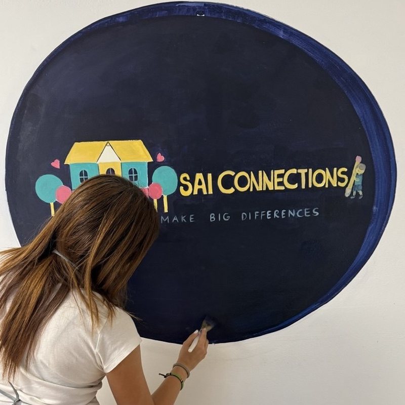 A member of the SAI Connections community hand-painting the SAI Connections logo mural on the wall of the center