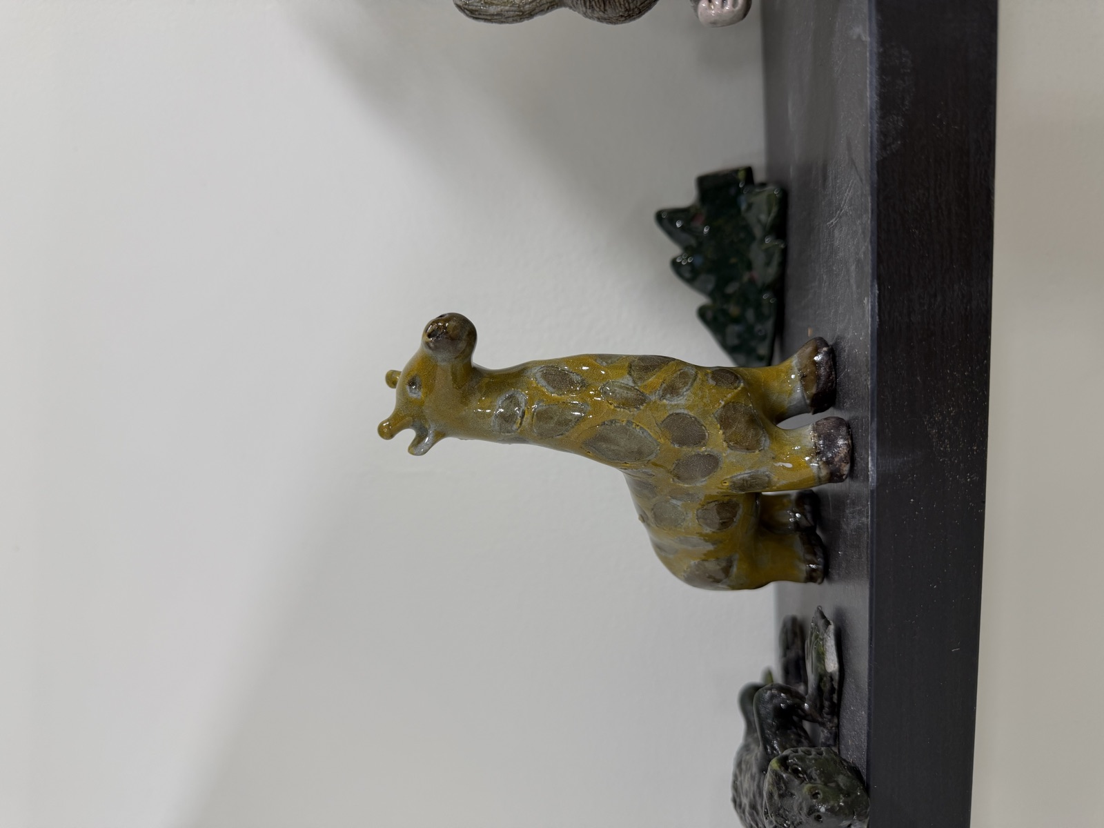 A hand-sculpted and painted clay giraffe standing on the studio shelf